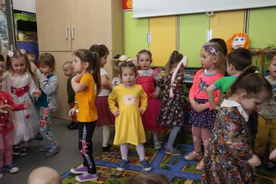 Dzieci tańczą, rece trzymają na biodrach, za nimi kolorowe mebelki.