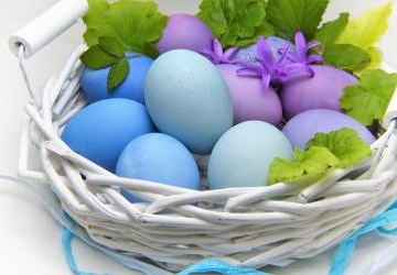 Kolorowe jajka w wiklinowym koszyku przyzdobione liśćmi mięty.