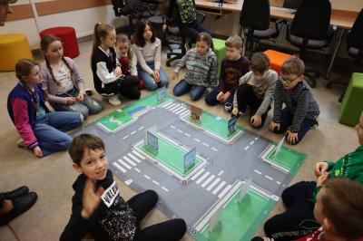 Dzieci siedzące wokół maty odwzorowującej miasto programują robota Photon oraz układają makietę budynków