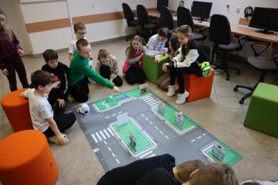 Dzieci siedzące wokół maty odwzorowującej miasto programują robota Photon oraz układają makietę budynków