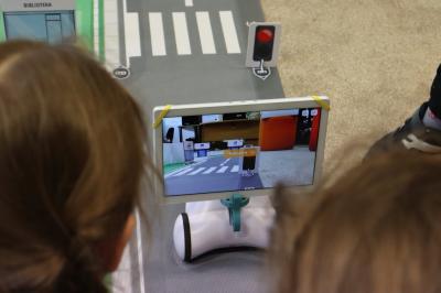 Dzieci siedzące wokół maty odwzorowującej miasto programują robota Photon oraz testują działanie sztucznej inteligencji.