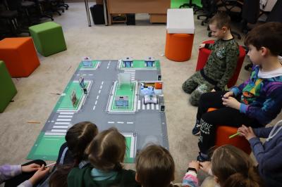 Dzieci siedzące wokół maty odwzorowującej miasto programują robota Photon oraz testują działanie sztucznej inteligencji.