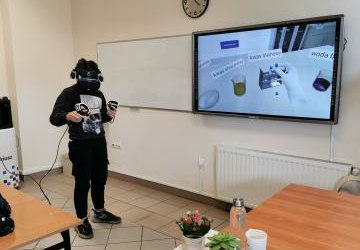 uczeń korzystając z gogli VR i kontrolerów wykonuje doświadczenie