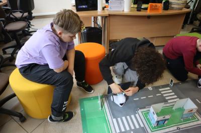 Uczniowie klasy VIb uczestniczą w zajęciach robotyki. Na dywanie rozłożone maty edukacyjna w raz z robotami.