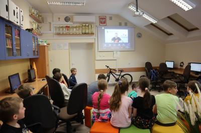 Uczniowie szkoły podstawowej biorący udział w warsztatach modelowania 3D na platformie Tinkercad. Uczestnicy spotkania oglądają obraz z projektora na którym widac trenera.