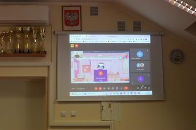 Uczniowie szkoły podstawowej biorący udział w warsztatach modelowania 3D na platformie Tinkercad. Uczestnicy spotkania oglądają obraz z projektora na którym widac trenera.