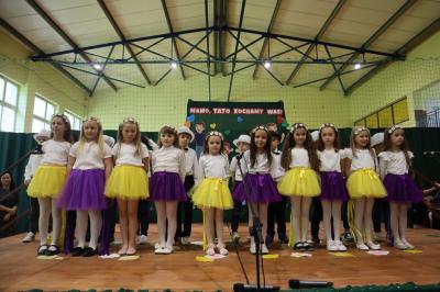 Dzieci z grupy Pszczółki stroją na scenie w dwóch rzędach - dziewczynki mają spódniczki zółte i fioletowe