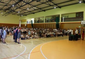 Uczniowie, rodzice oraz nauczyciele zgromadzeni w hali gimnastycznej podczas uroczystości zakończenia roku szkolnego.