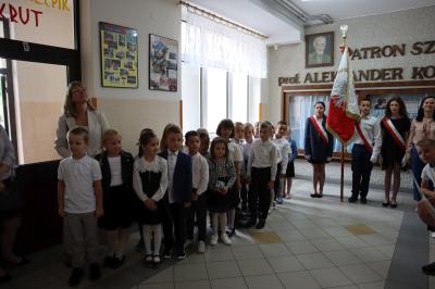 Klasa pierwsza stoi na baczność podczas odśpiewania hymnu państwowego. W tle poczet sztandarowy.