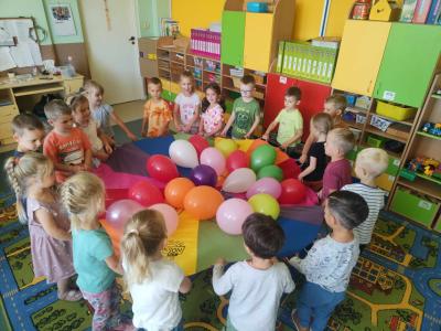 Przedszkolaki trzymające kolorową hustę z balonami w środku.