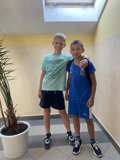 Dwóch uczniów ubranych na niebiesko stoi na szkolnym korytarzu.