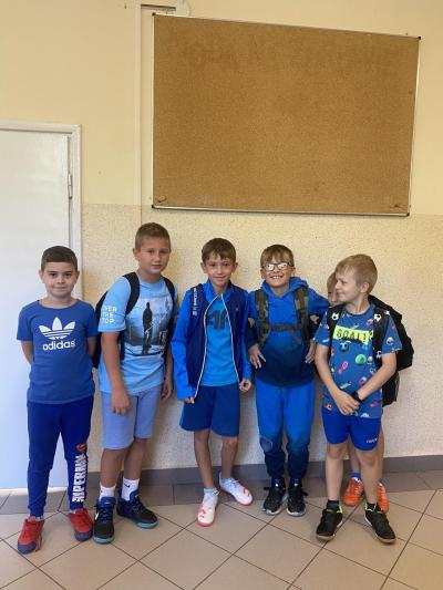 Grupa chłopców z klasy 4b w niebieskich ubraniach stoi na szkolnym korytarzu.
