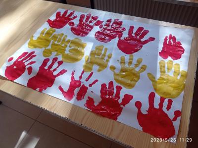 Plakat z odciśniętymi dłońmi uczniów w kolorach flagi hiszpańskiej czerwonym i żółtym.