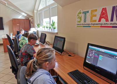 Dzieci siedzą przy komputerach i poprzez stronę code.org kodują gry