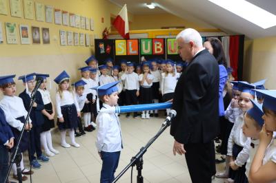 Dyrektor szkoły pan Aleksander Kalisz pasuje uczniów klas pierwszych ołówkiem.