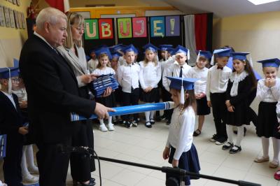 Dyrektor szkoły pan Aleksander Kalisz pasuje uczniów klas pierwszych ołówkiem.