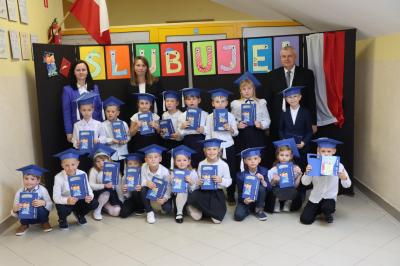Zdjęcie grupowe klasy Ia. Dzieci prezentują pamiątkowe dyplomy, stojąc wraz wychowawczyniami oraz panem dyrektorem