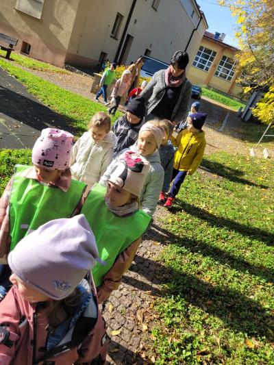 Przedszkolaki spacerują chodnikiem zbierając liście.