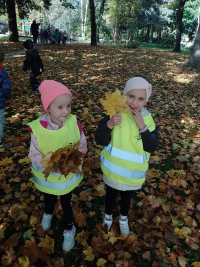 Grupa Leśne duszki w parku bieckim. dwie dziewczynki ubrane w kamizelki odblaskowe pokazują do kamery swoje zdobycze, czyli ciekawe jesienne listki