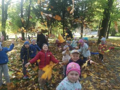 Grupa sówki w parku. dzieci podrzucają kolorowe liście i uśmiechaja się do kamery.