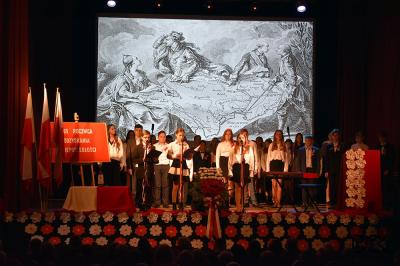 Uczniowie ZSP prowadzą uroczystą akademię na scenie. W tle wyświetlana mapa Polski.