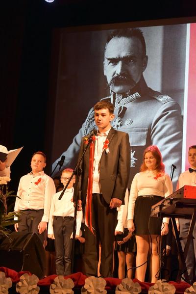 Uczniowie ZSP prowadzą uroczystą akademię na scenie. W tle zdjęcie marszałka Józefa Piłsudskiego.