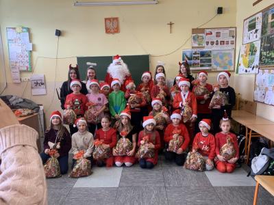 Święty Mikołaj wraz z aniołkami pozuje do zdjęcia grupowego wraz z uczniami.