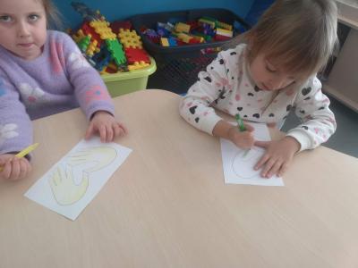 Dzieci siedzą przy stole i kolorują kredkami szablon ,,Serce na dłoni”