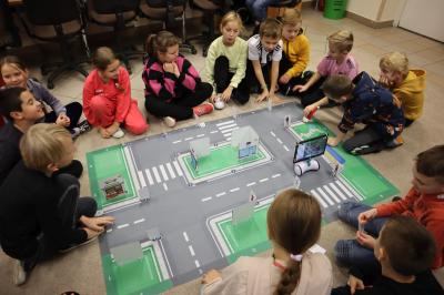 Uczniowie siedzą wokół maty i programują robota Photon.
