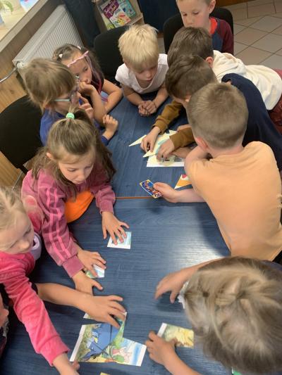 Dzieci zgromadzone przy stole układają puzzle z porozcinanych obrazków.