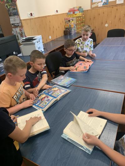Dzieci zgromadzone przy stole w bibliotece szkolnej ogladają książki..