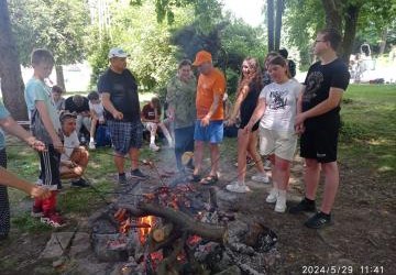 Grupowe zdjęcie przy ognisku podczas pieczenia kiełbasek.