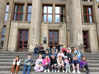 dzieci siedzą na schodach za nimi gmach budynku na którym widnieje napis- Muzeum Narodowe w Krakowie