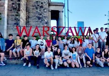 grupa uczniów pozuje do zdjęcia na tle napisu Warszawa