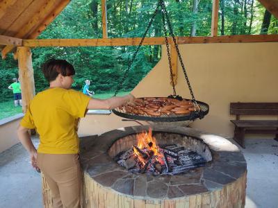 Pani stoi przy grillu, obraca szczypcami kiełbaski.