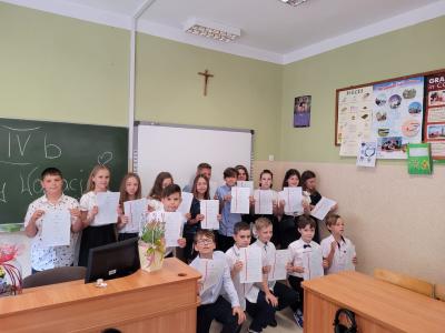 Klasa czwarta stoi w sali lekcyjnej ze świadectwami na koniec roku szkolnego.