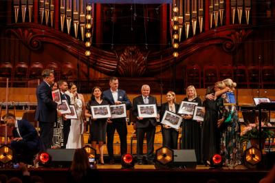 Grupa osób stojąca na scenie Filharmonii Narodowej z pamiątkowymi zdjęciami.