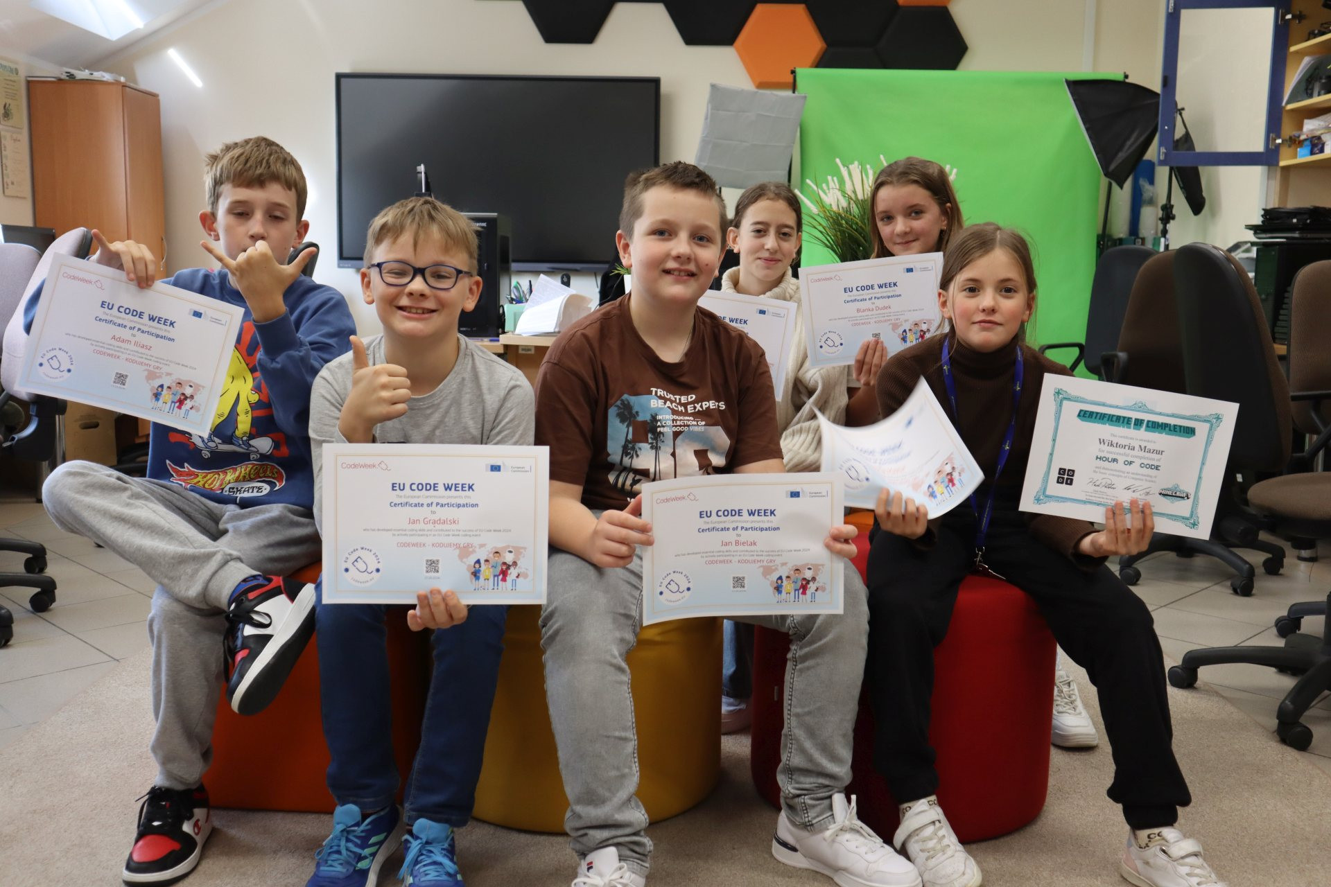 Uczniowie siedzą na pufach i prezentują otrzymane certyfikaty CodeWeek