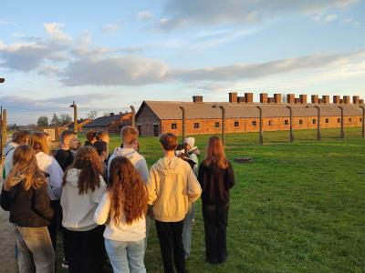 Grupa uczniów z przewodnikiem na tle budynków obozu w Birkenau