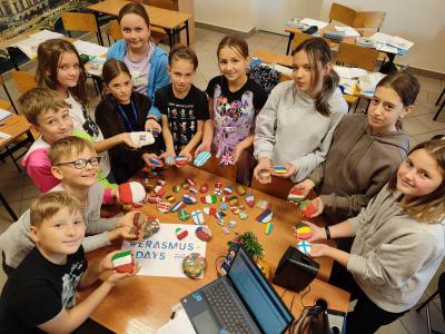 Grupa uczniów prezentuje wykonane flagi na kamykach.