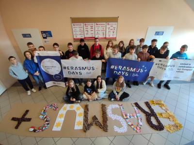 Grupa uczniów z banerami Erasmus + a przed nimi duży napi Erasmus +