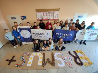 Grupa uczniów z banerami Erasmus + a przed nimi duży napi Erasmus +