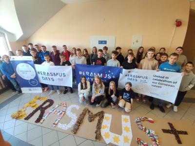 Grupa uczniów z banerami Erasmus + a przed nimi duży napi Erasmus +