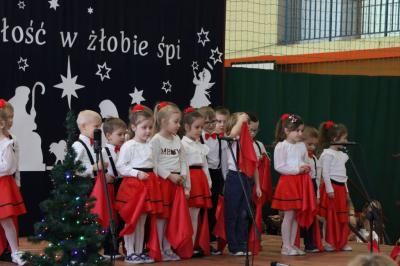 Grupka dzieci stoi na scenie. Mają biało-czerwone ubranka, w rękach trzymają czerwone chustki..