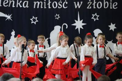 Grupka dzieci tańczy na scenie. Mają biało-czerwone ubranka, w rękach trzymają czerwone chusteczki.