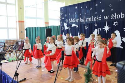 Grupka dzieci tańczy na scenie. Mają biało-czerwone ubranka, w rękach trzymają czerwone chustki