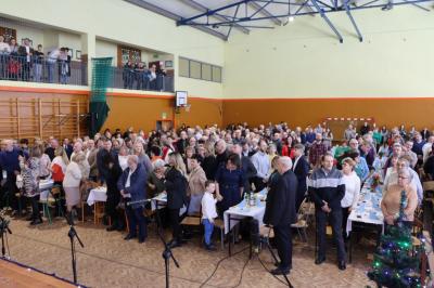 Zebrani goście - babcie i dziadkowie siedzący przy stołach w hali sportowej.