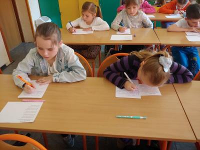 Dzieci biorące udział w szkolnym konkursie kaligrafii przepisują tekst wiersza na kartkę