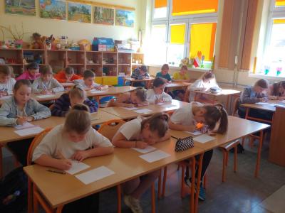 Dzieci biorące udział w szkolnym konkursie kaligrafii przepisują tekst wiersza na kartkę