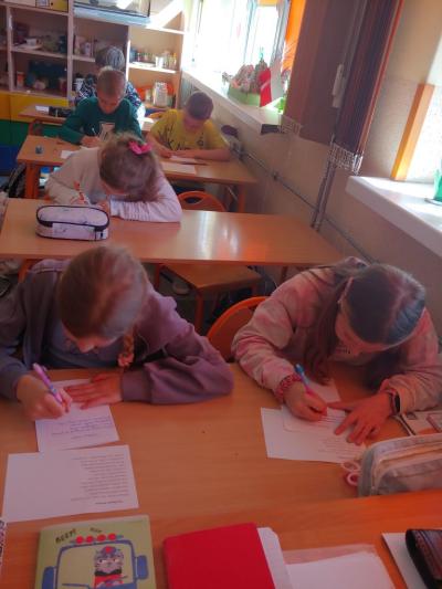 Dzieci biorące udział w szkolnym konkursie kaligrafii przepisują tekst wiersza na kartkę